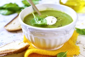 Spinach creamy soup in a white bowl on light background.