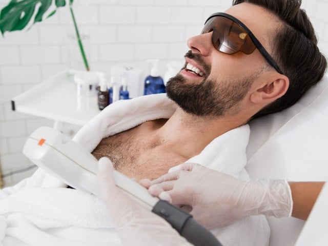 bearded man sitting in laser safety goggles in spa salon