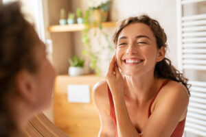 Smiling woman uses cotton pad to cleanse face in mirror for acne treatment and clear skin